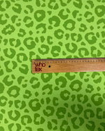 Close-up of neon green leopard print fabric with a wooden ruler measuring the pattern size