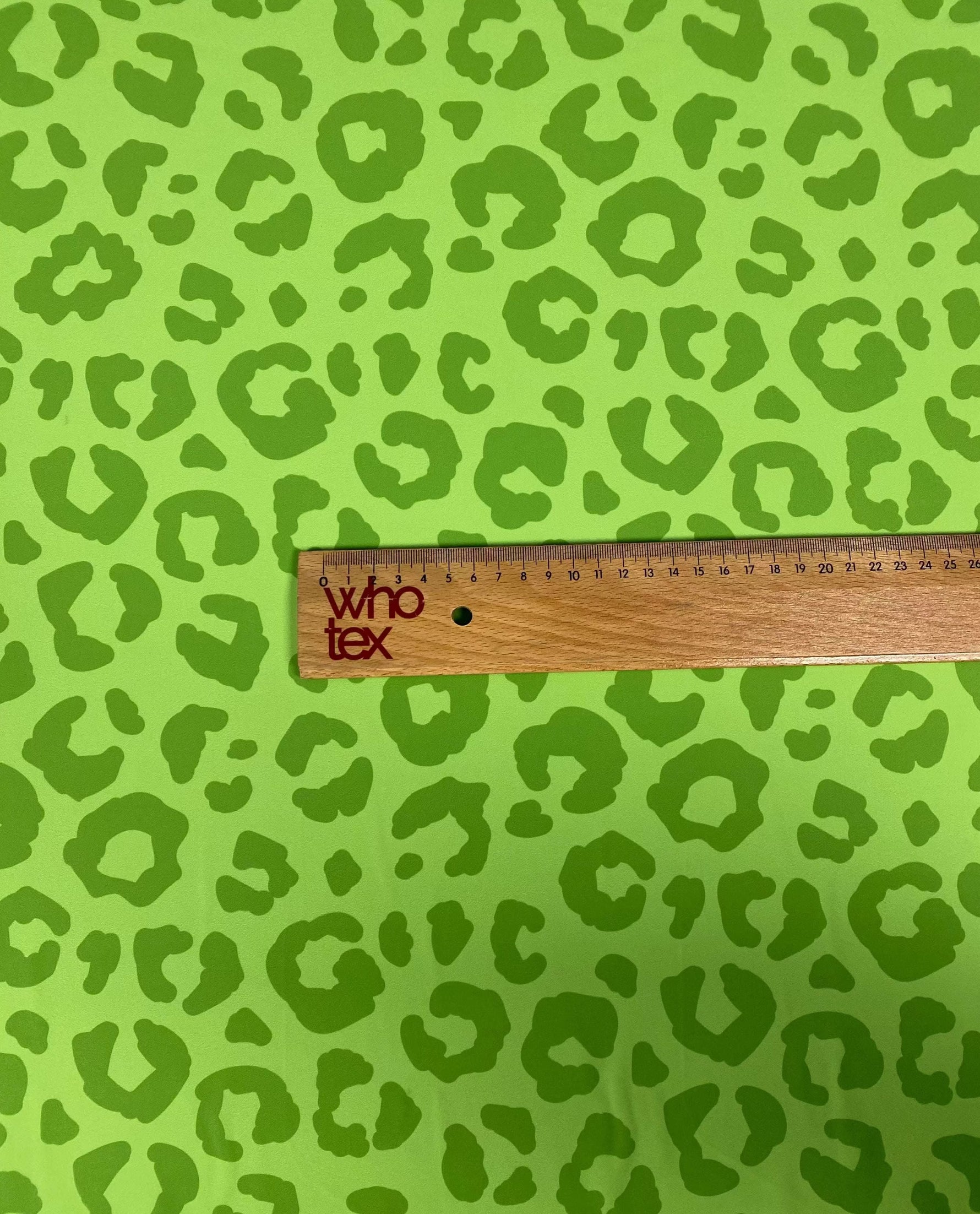Close-up of neon green leopard print fabric with a wooden ruler measuring the pattern size