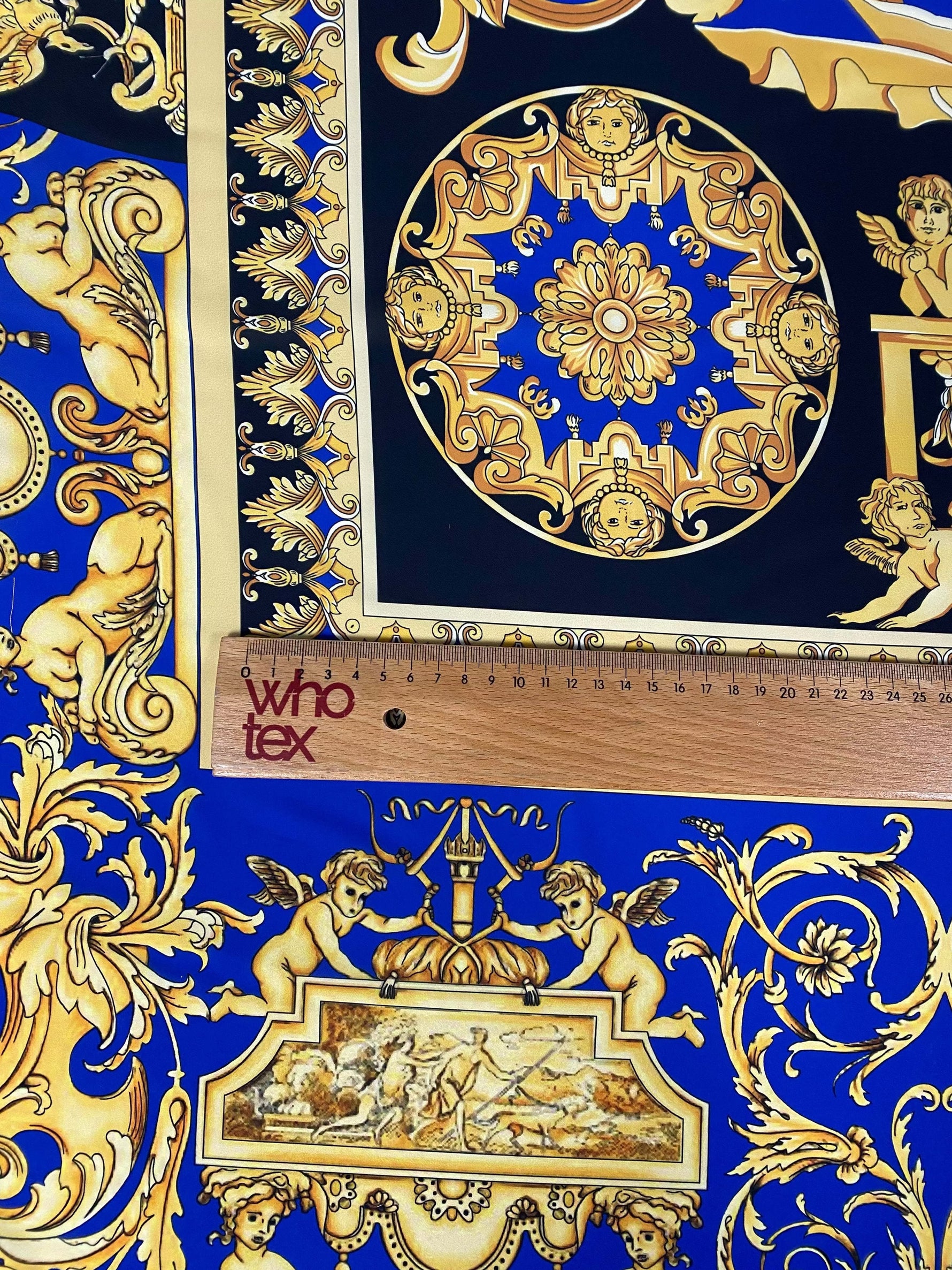 Royal blue baroque fabric with intricate gold patterns and cherub motifs, shown with ruler for scale