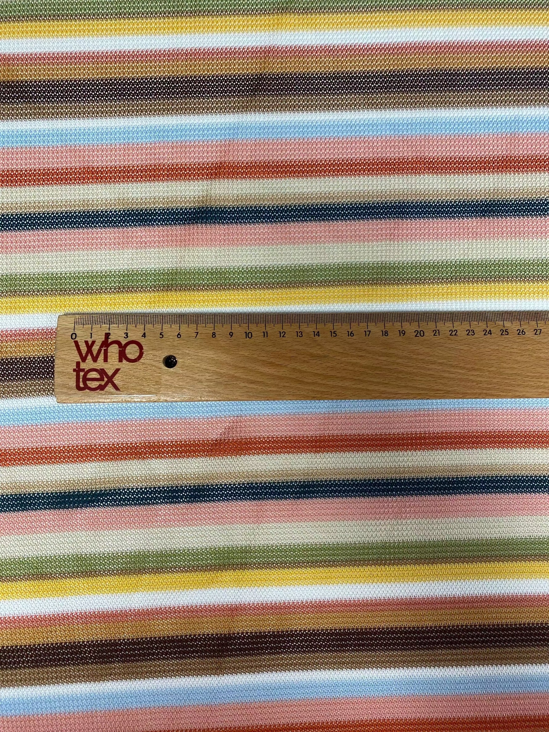 Multicolor striped woven fabric with zigzag knit pattern in green, blue, pink, yellow, and brown tones with ruler for scale