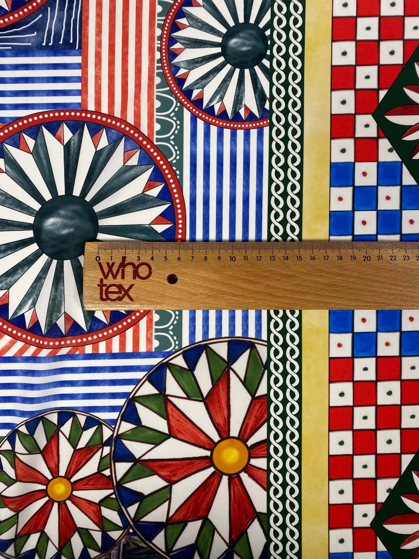 Sicilian Caretto Pattern Fabric with vibrant geometric and floral designs in red, blue, green, and yellow colors, measured with a wooden ruler.