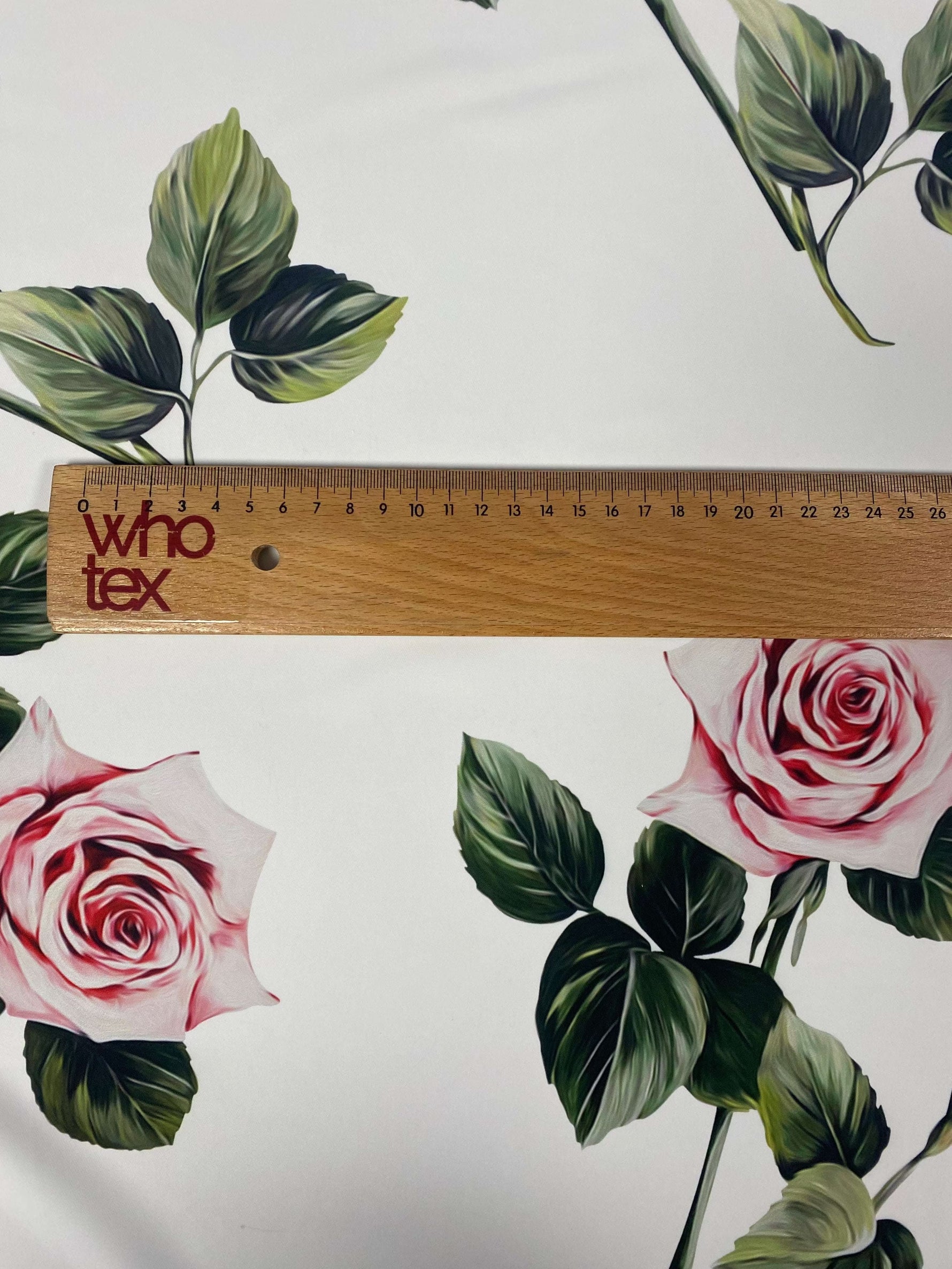 Pink rose floral fabric on white background with green leaves and ruler for scale