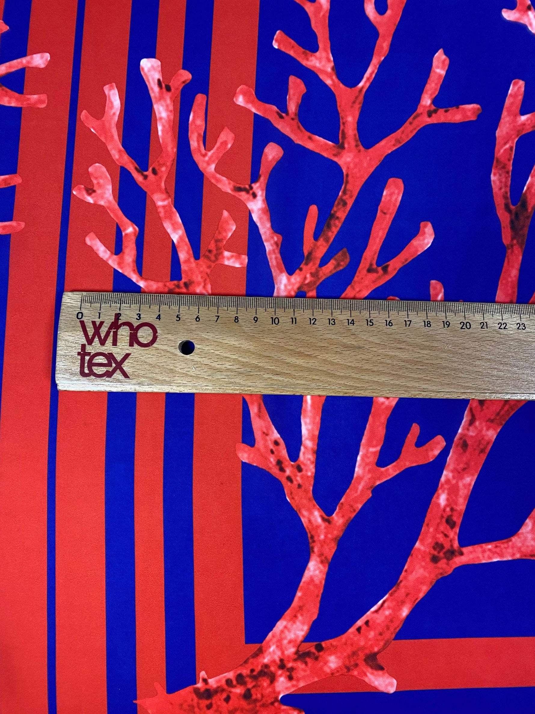 Red coral pattern fabric panel with navy blue background and ruler for scale