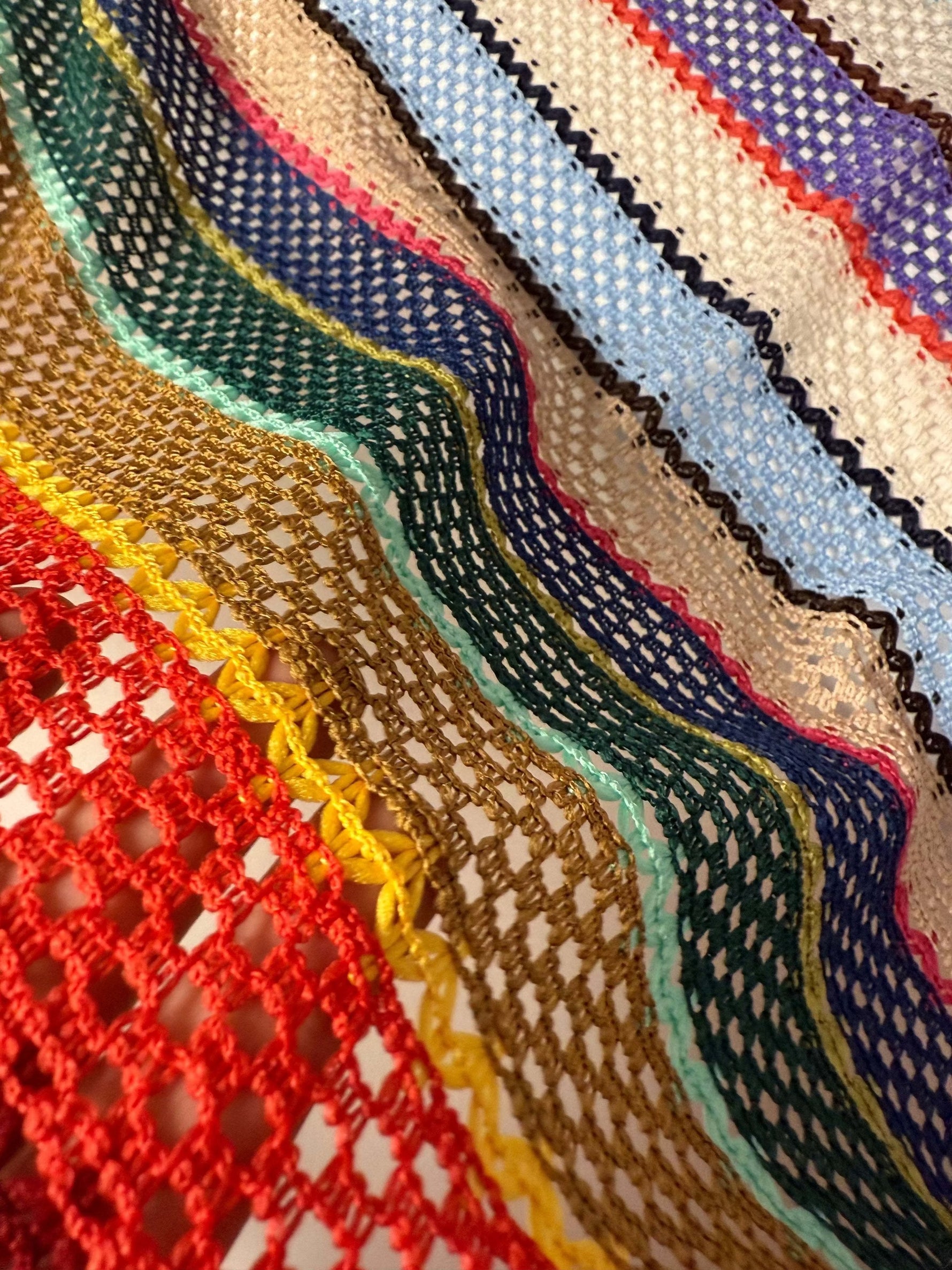 Close-up of colorful knit mesh fabric with zigzag striped pattern in green, red, blue, yellow, and beige tones