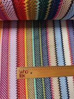 Colorful knit mesh fabric with striped zigzag pattern in various vibrant colors and a wooden ruler for scale