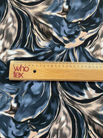 Close-up of abstract feather pattern fabric in black, beige, and blue with ruler for scale