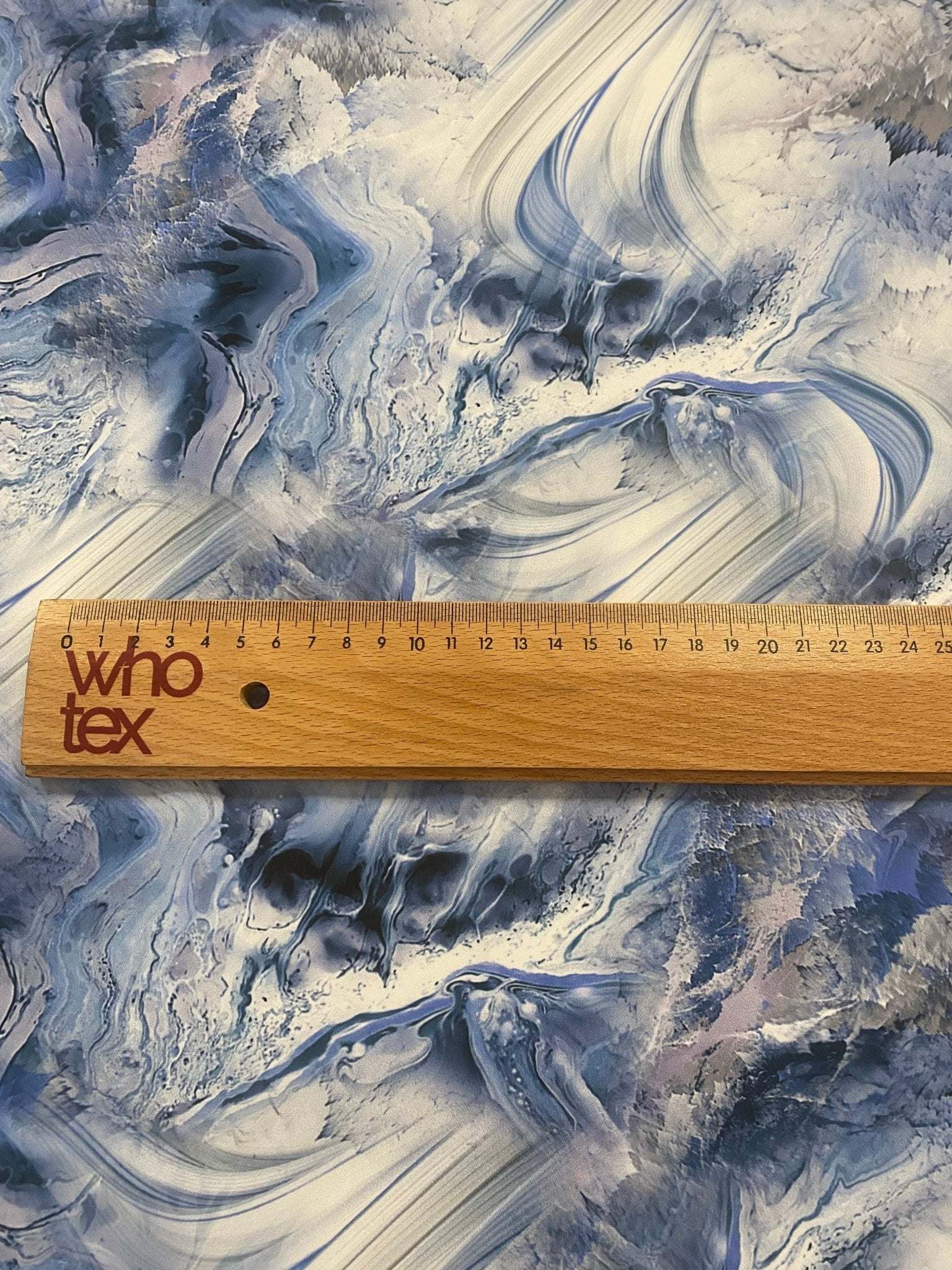 close up of abstract marble effect fabric with blue and white swirls and a wooden ruler showing scale