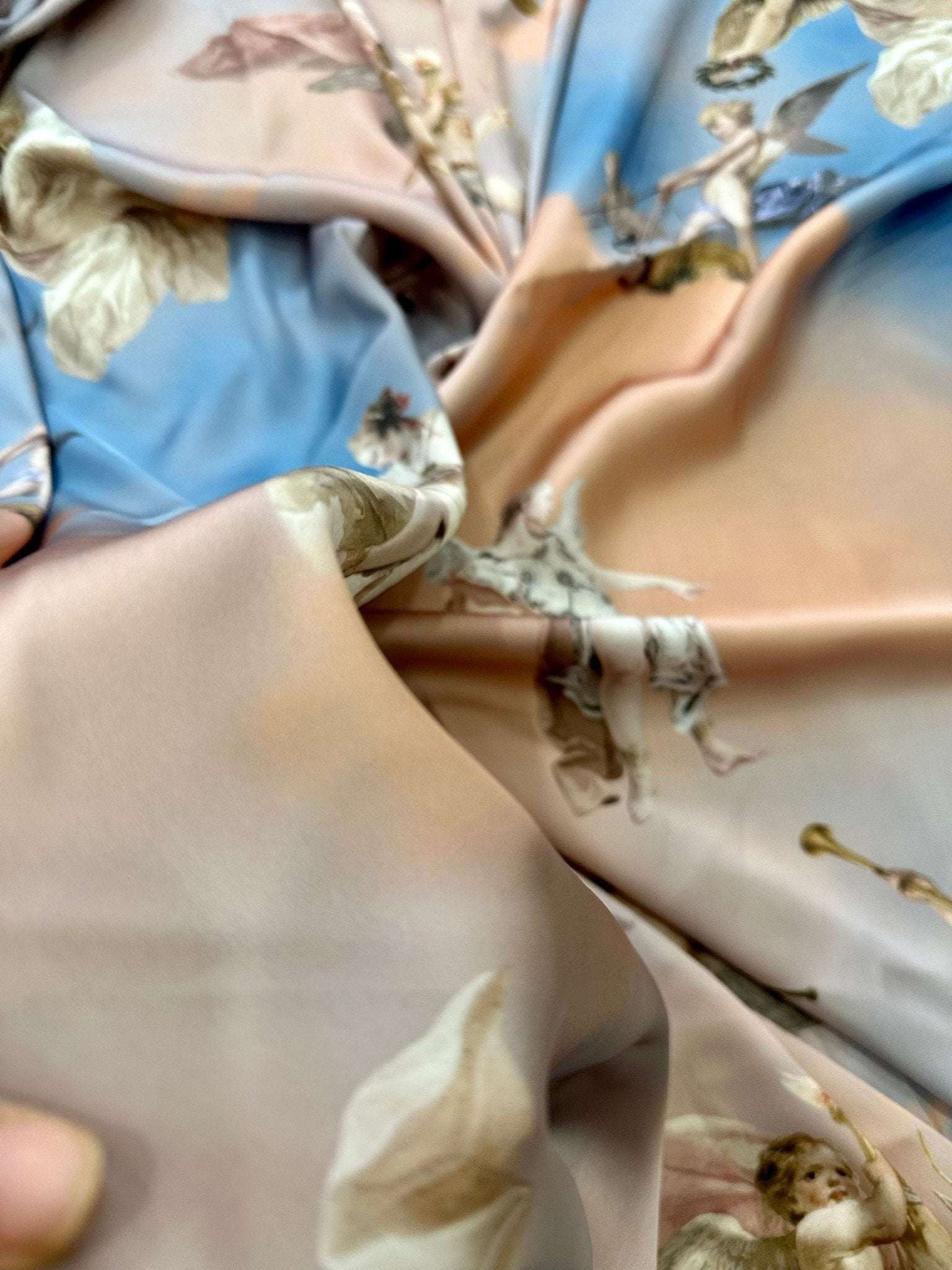 Soft angel print fabric in sky blue and pastel tones with whimsical cloud and cherub designs