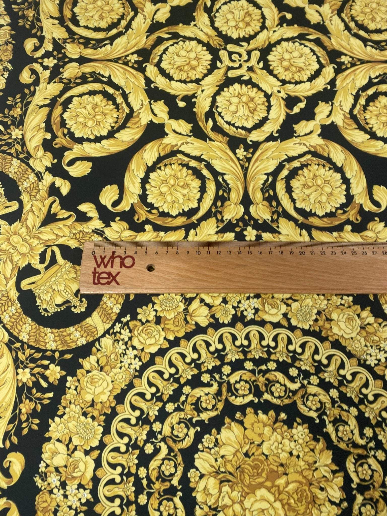Baroque black and gold upholstery fabric with ornate floral and scroll patterns and a measuring ruler for scale