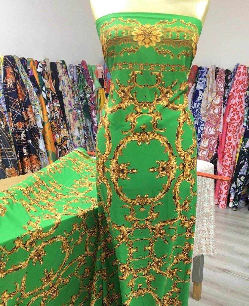 Baroque fabric with green background and intricate gold print displayed on a mannequin and table in fabric store