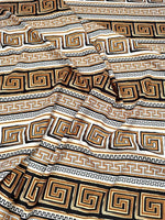 Beige brown silky crepe fabric with geometric black and gold pattern, soft and smooth texture, ideal for elegant garments