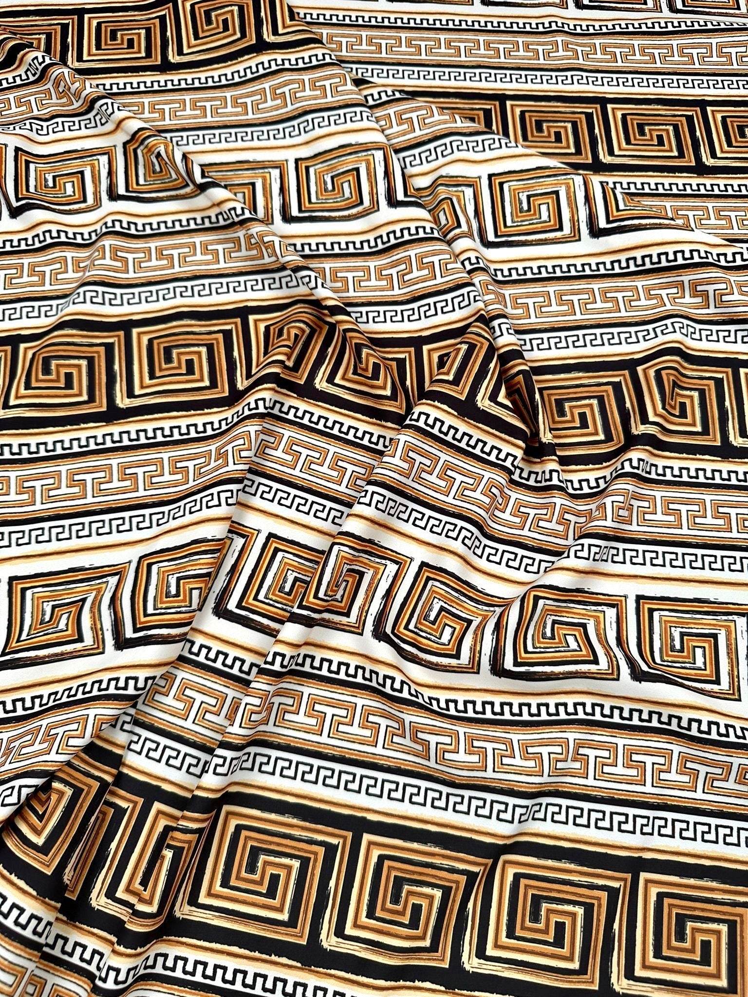 Beige brown silky crepe fabric with geometric black and gold pattern, soft and smooth texture, ideal for elegant garments