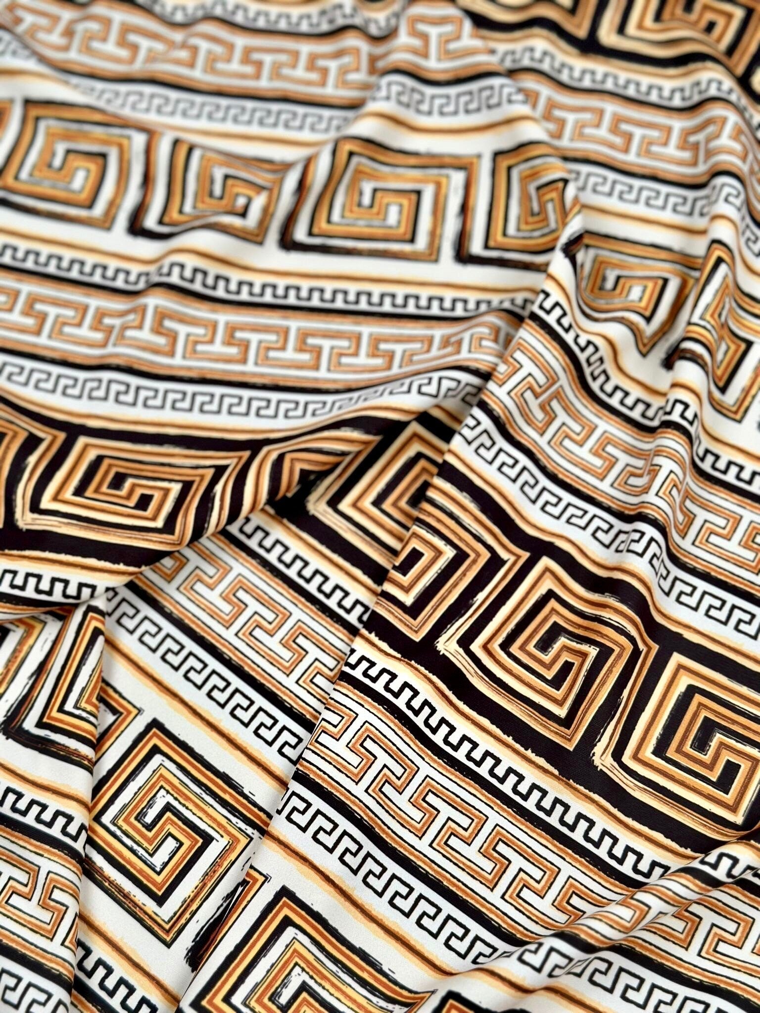 Beige brown silky crepe fabric with geometric and Greek key patterns, smooth and draping textile ideal for garments