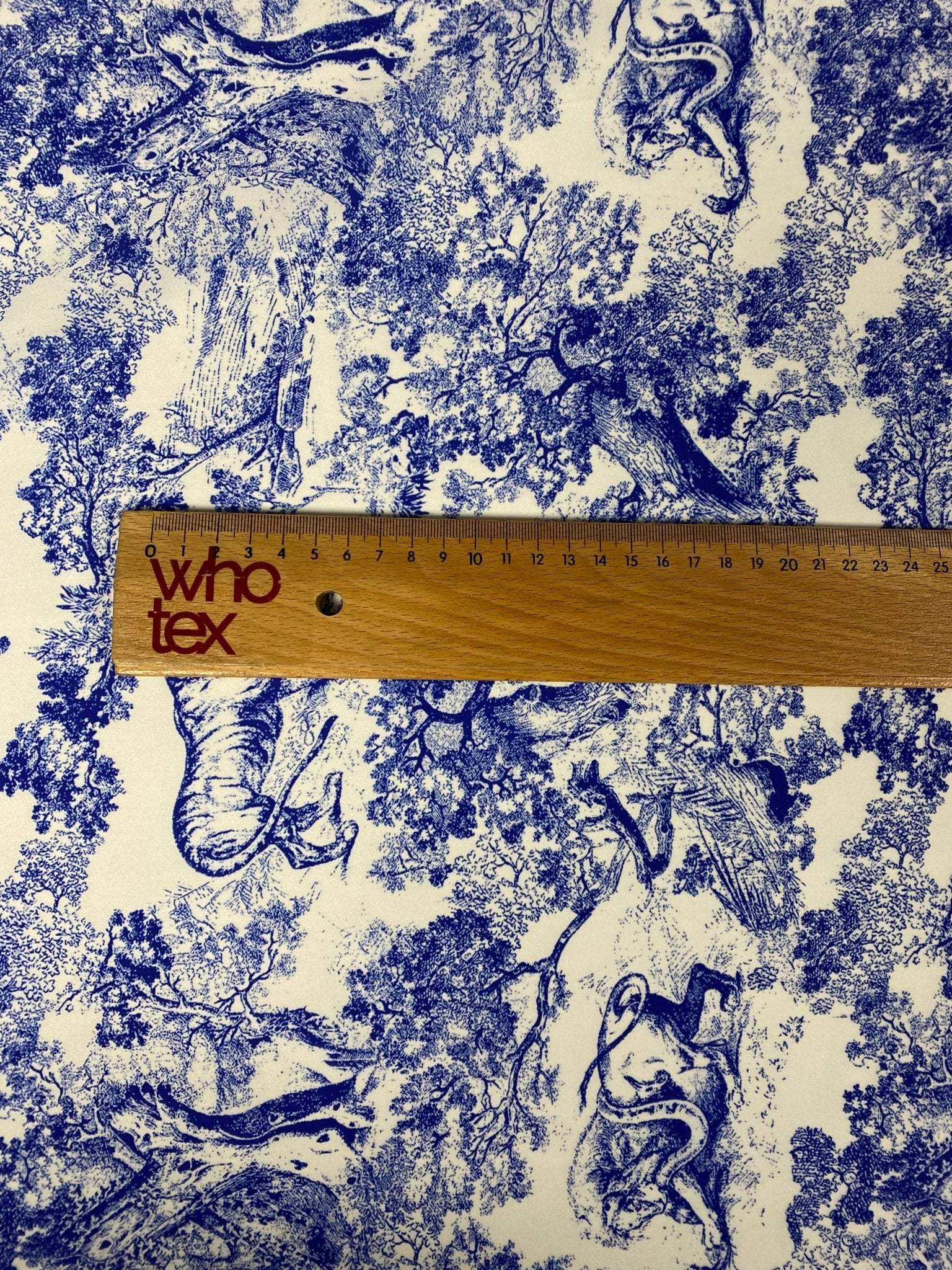 Blue fabric with detailed wild forest pattern featuring trees and animals, ruler for scale