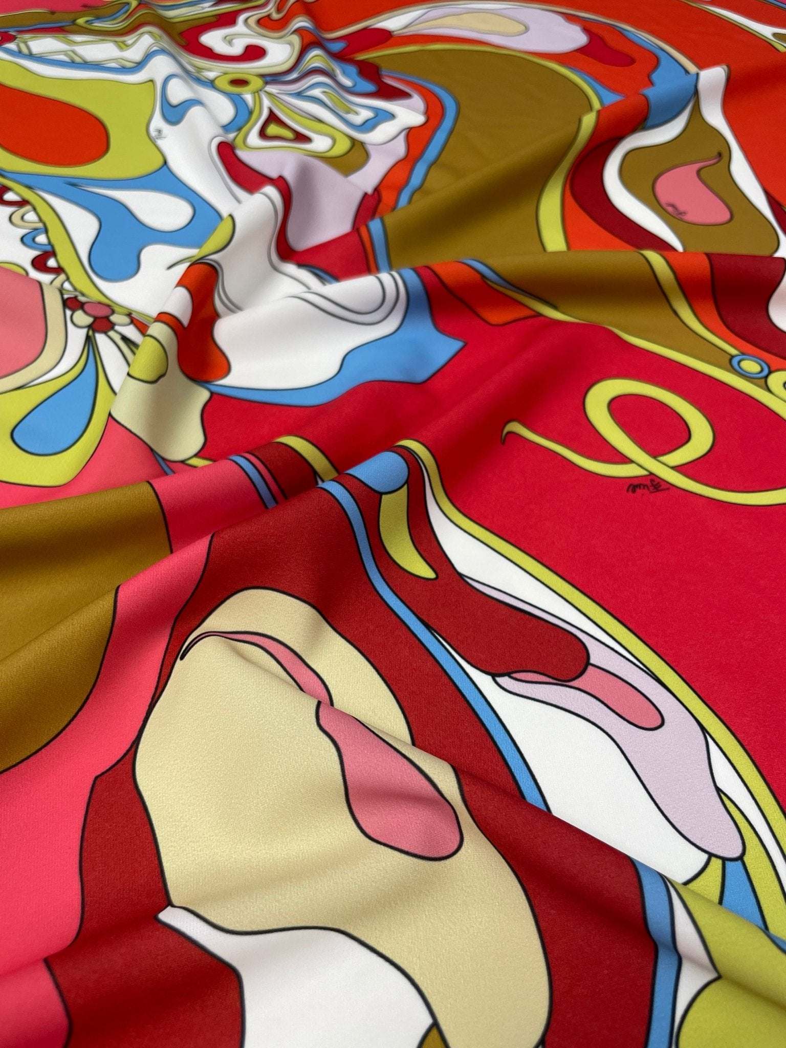 Vibrant colorful abstract swirl pattern fabric with red, blue, pink, white, and gold hues and fluid shapes
