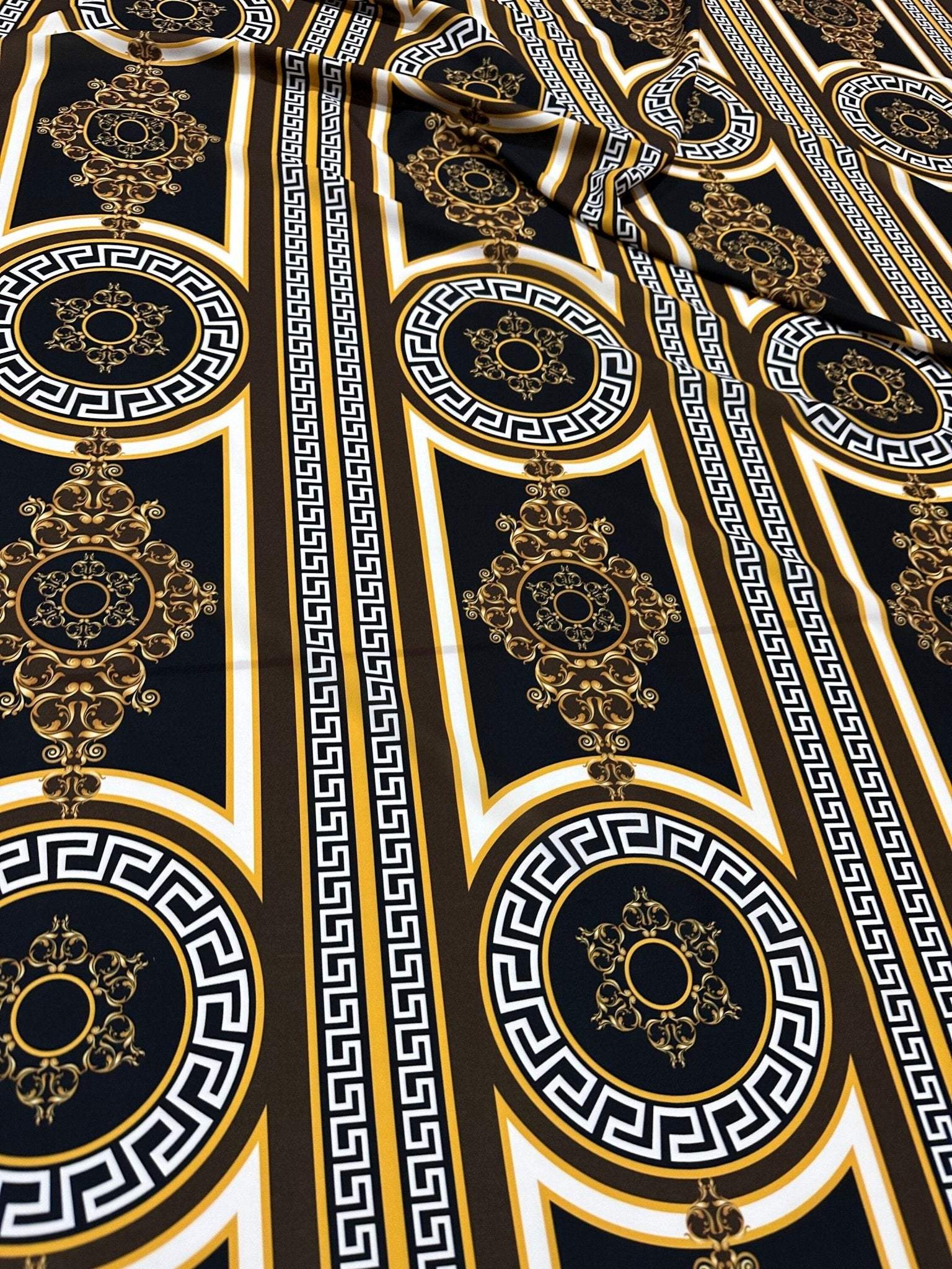 Brown silky crepe fabric with Greek key pattern and ornate circular designs in black, white, and gold tones.