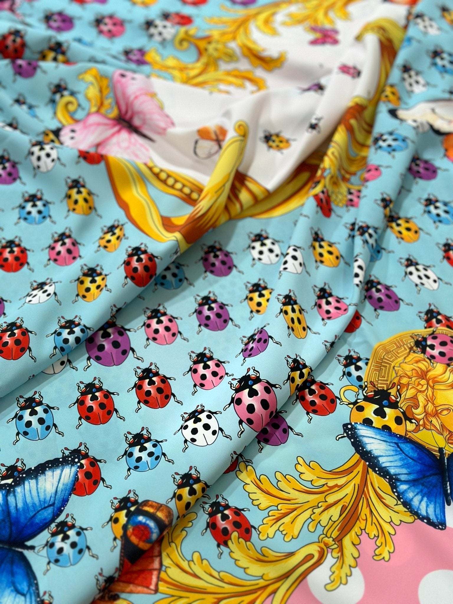 Colorful butterfly and ladybug pattern fabric with polka dot border and vibrant blue background