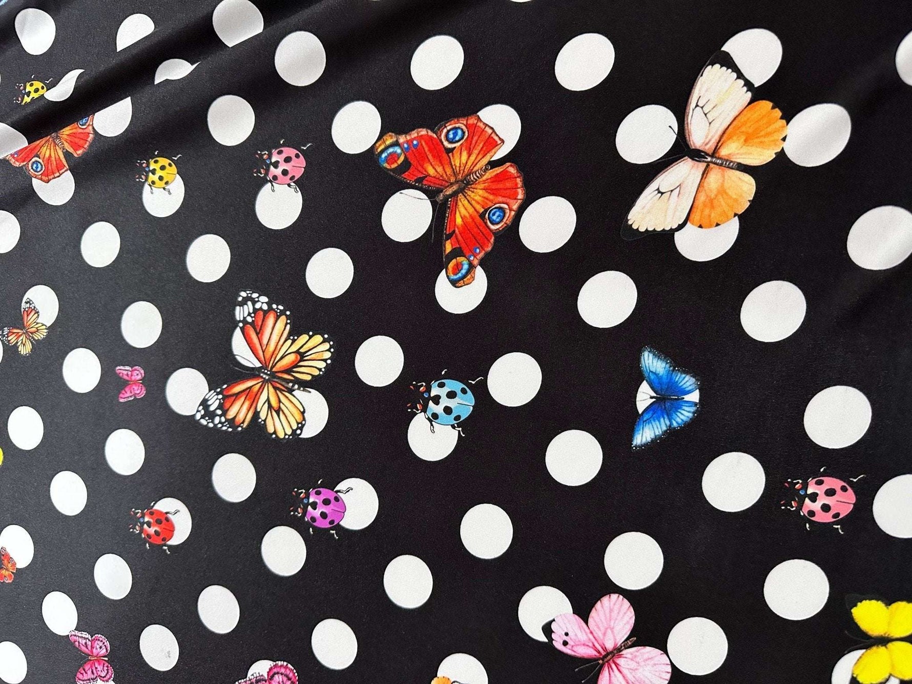 Black fabric with white polka dots and colorful butterfly and ladybug prints for sewing projects