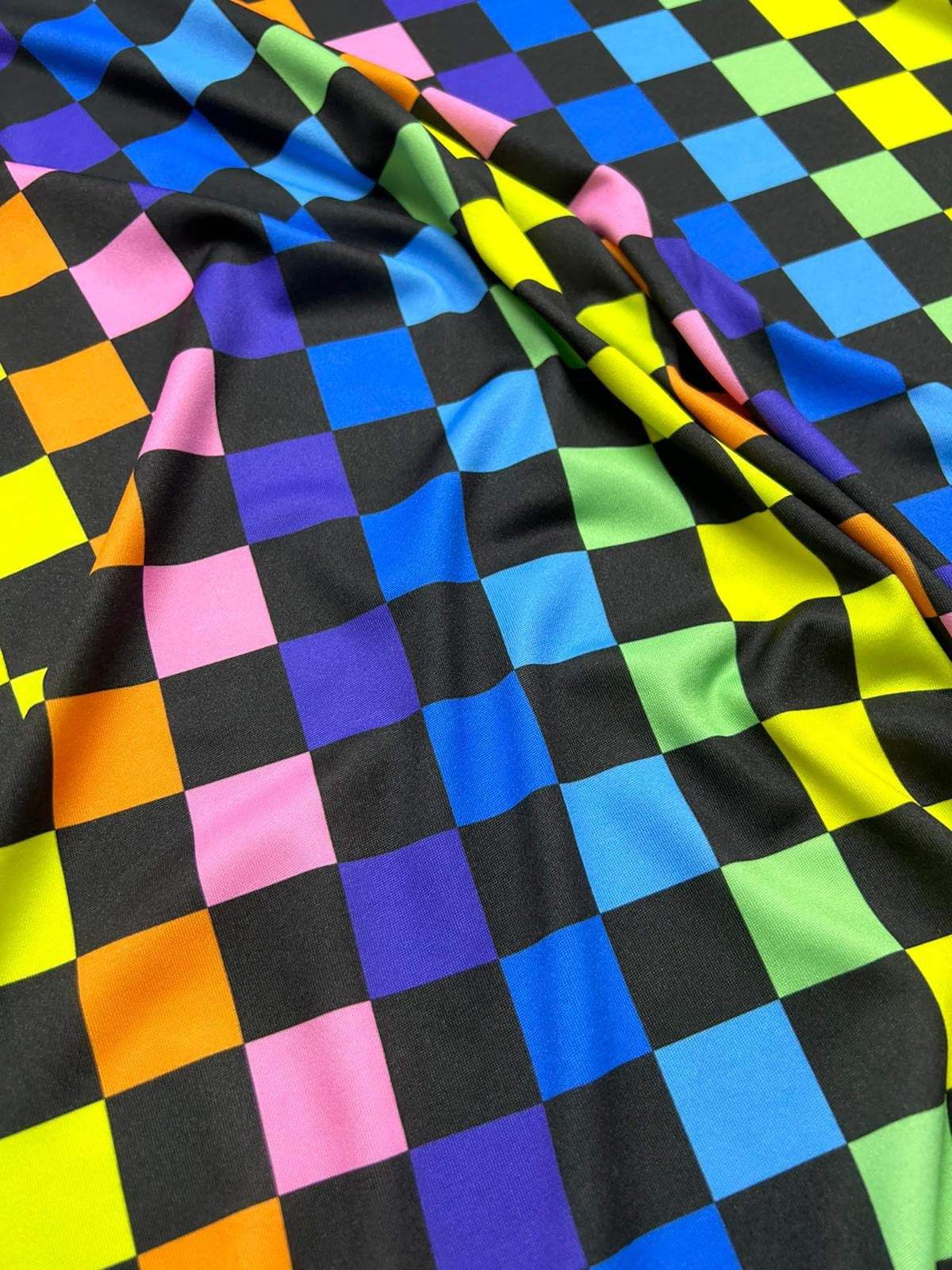 Rainbow checkers print fabric with vibrant multicolor squares on a black background, ideal for sewing projects and crafts