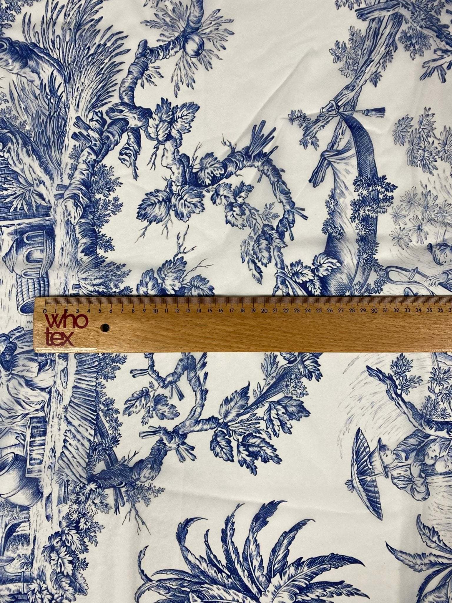 Classic blue Toile de Jouy print fabric with detailed classic pastoral scenes and foliage on white background, ruler showing scale