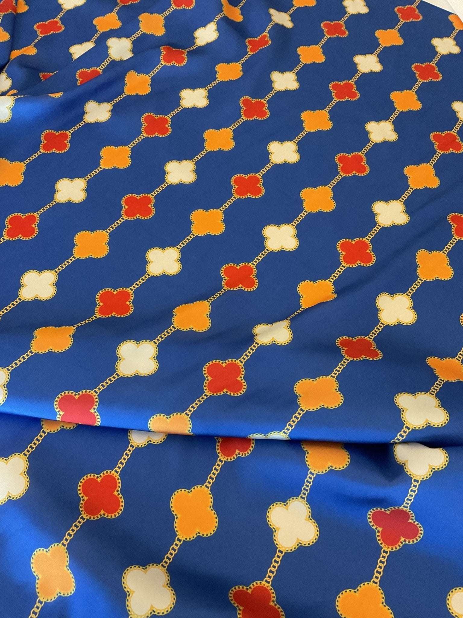 Navy blue fabric with orange, red, and white clover chain pattern for sewing and apparel projects