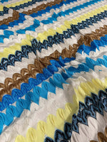 Close-up of colorful chevron embroidered fabric with zigzag knit pattern in green, blue, yellow, brown, and white tones.