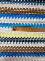 Close-up of colorful chevron embroidered fabric with zigzag knit pattern in blue, brown, yellow, white, and black tones with a wooden ruler for scale