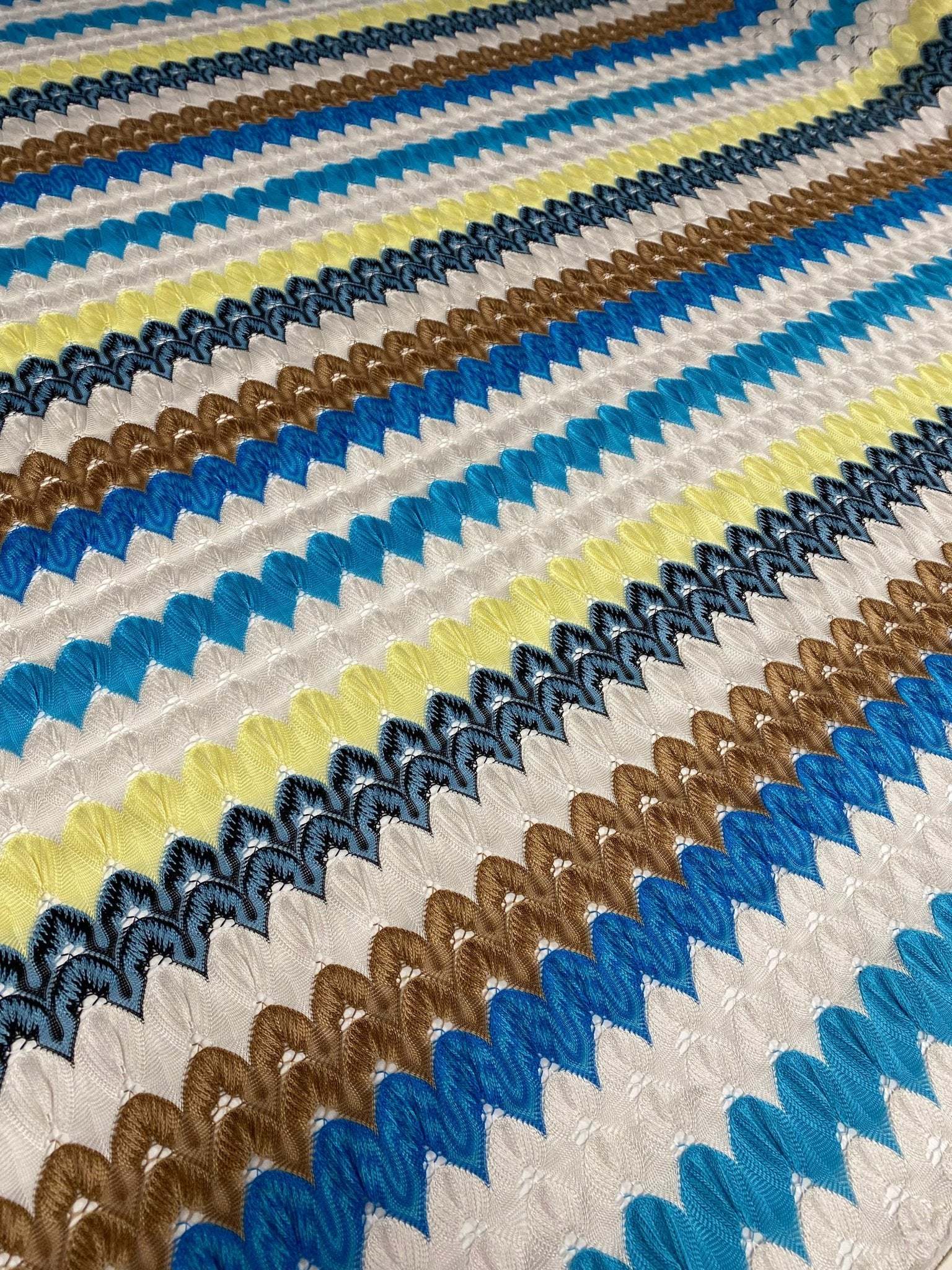 Colorful chevron embroidered fabric with green, blue, brown, and yellow zigzag knit pattern for sewing projects