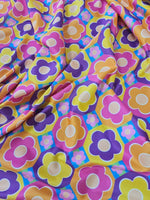 Colorful floral fabric with vibrant pink, yellow, orange, and purple flower patterns on a blue background, sold by the yard and 150cm wide