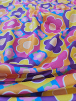 colorful floral fabric with vibrant flower patterns in pink, purple, yellow, and orange hues on a smooth textile background