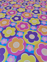 Colorful floral fabric with vibrant flowers in purple, yellow, orange, and pink on a multicolor geometric background
