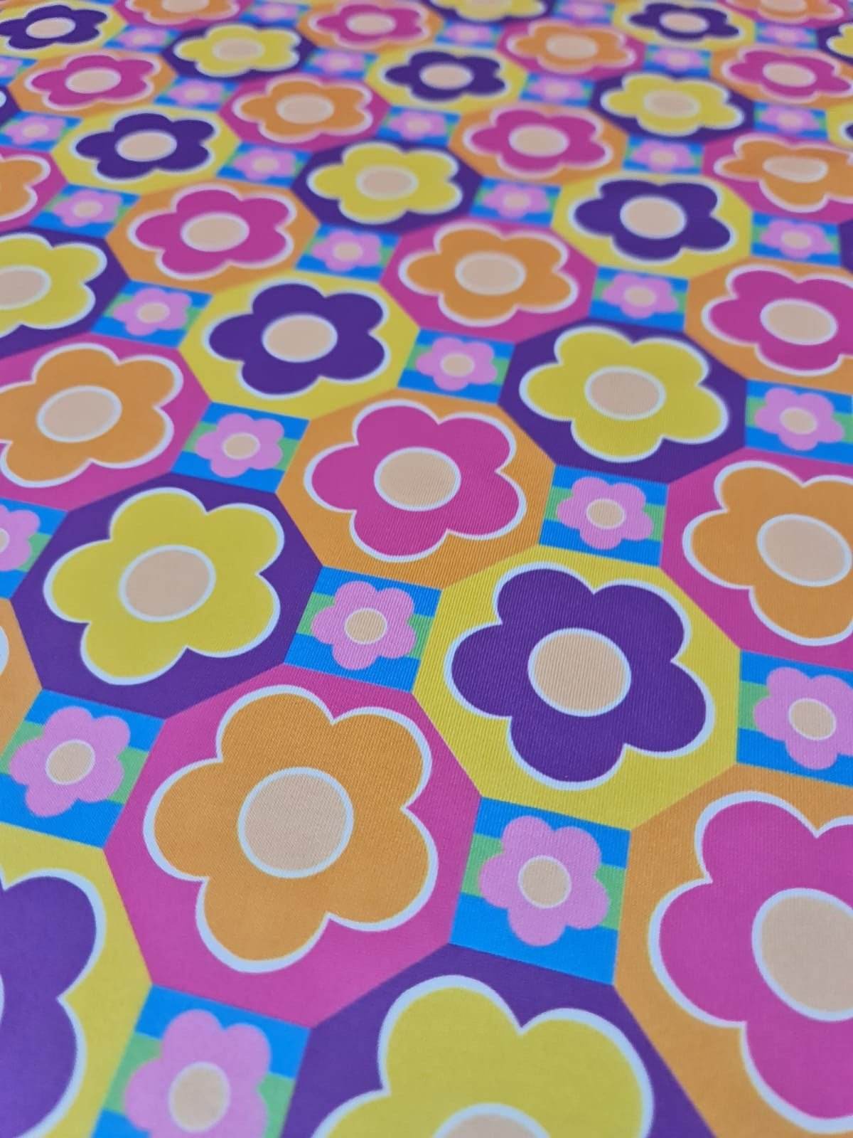 Colorful floral fabric with vibrant flowers in purple, yellow, orange, and pink on a multicolor geometric background