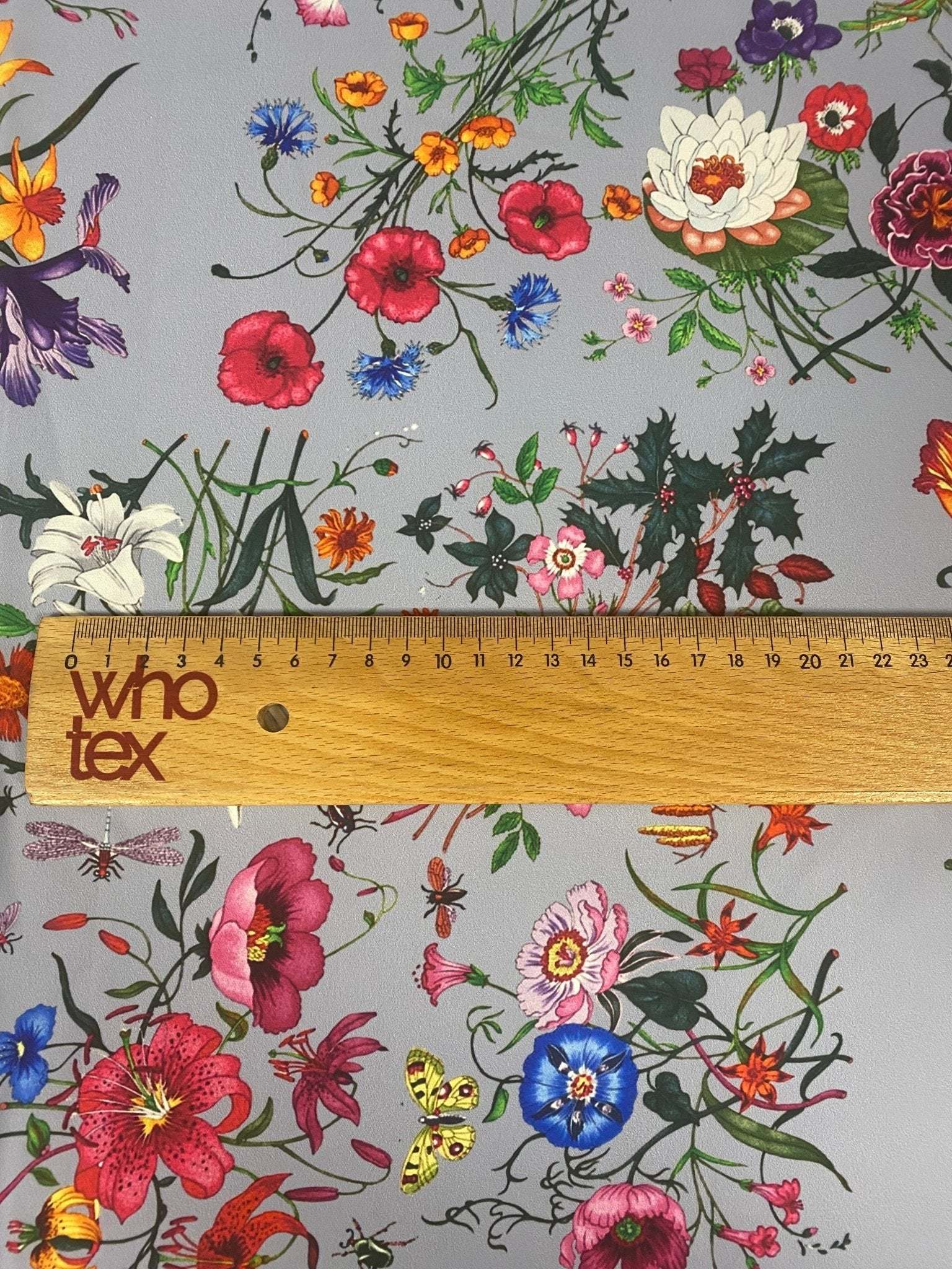 Colorful floral pattern fabric on light grey background with vibrant flowers and greenery, ruler showing fabric width of 150cm
