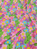 Colorful floral fabric with vibrant pink, blue, purple, and yellow flowers and green leaves pattern for sewing projects
