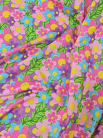 Bright colorful floral fabric with pink, blue, purple, and yellow flowers and green leaves, perfect for sewing projects