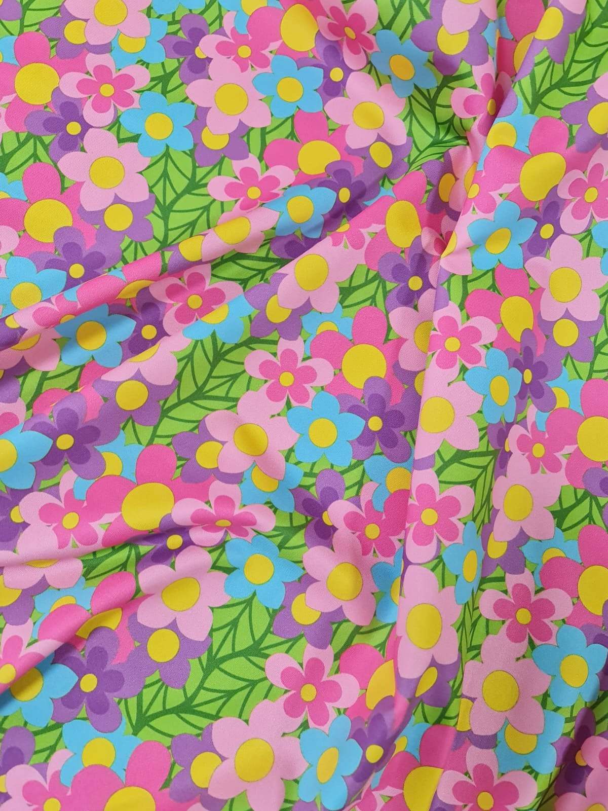 Bright colorful floral fabric with pink, blue, purple, and yellow flowers and green leaves, perfect for sewing projects