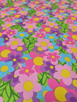 Colorful floral fabric with vibrant pink, purple, blue, and yellow flowers and green leaves pattern