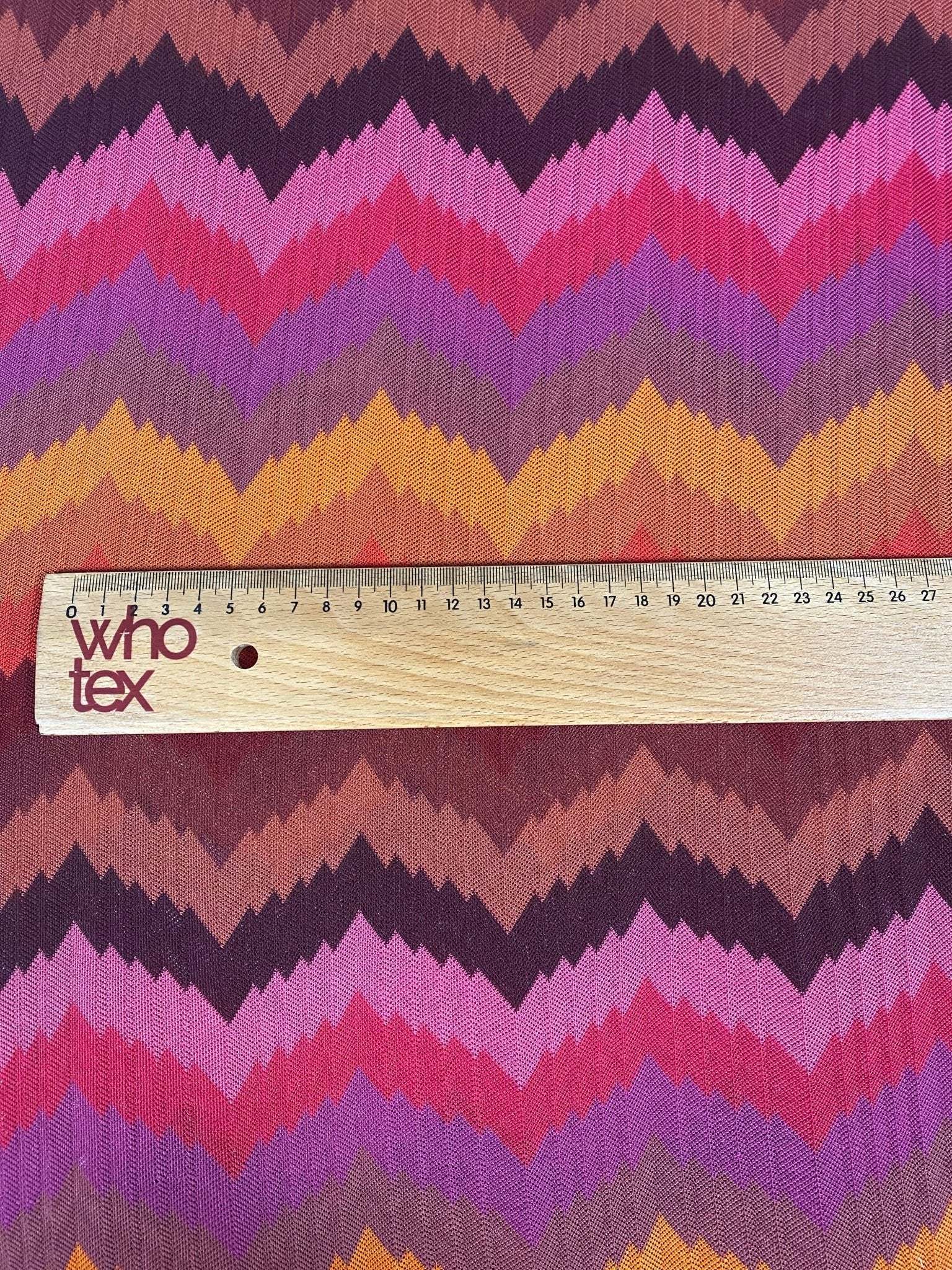 Colorful zigzag chevron pattern knit fabric in green, pink, purple, and yellow tones with ruler for scale