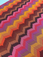 Colorful zigzag chevron pattern fabric with vibrant tones of orange, pink, purple, brown, and yellow in a knit texture