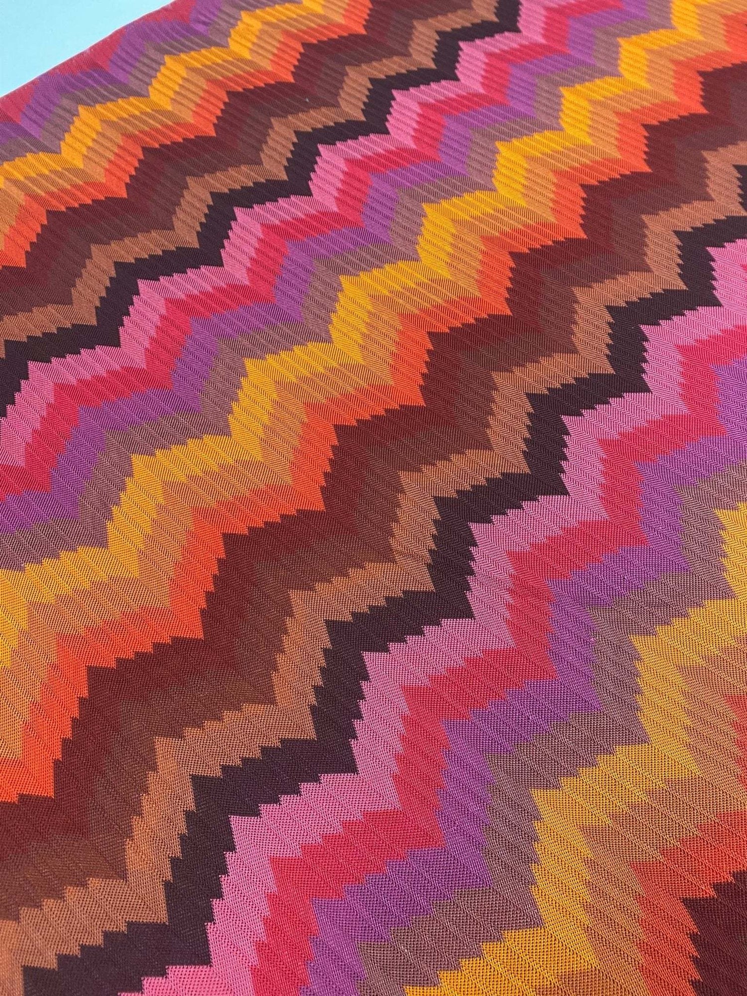 Colorful zigzag chevron pattern fabric with vibrant tones of orange, pink, purple, brown, and yellow in a knit texture