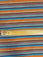 Colorful zigzag stripe knit fabric in green, orange, blue, and brown tones with a wooden ruler for scale