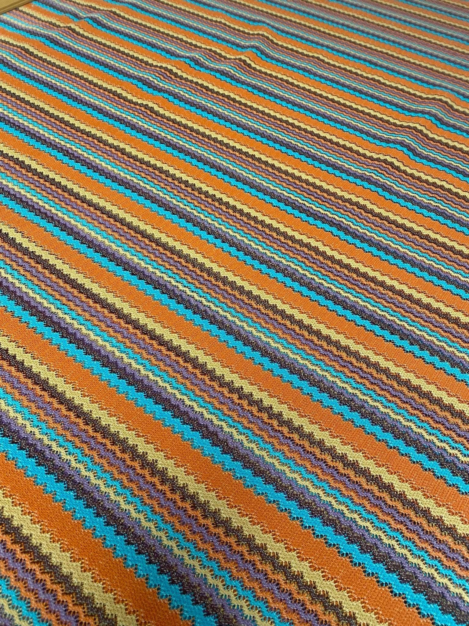 Colorful zigzag stripe knit fabric with vibrant green, orange, blue, and brown tones in a continuous pattern
