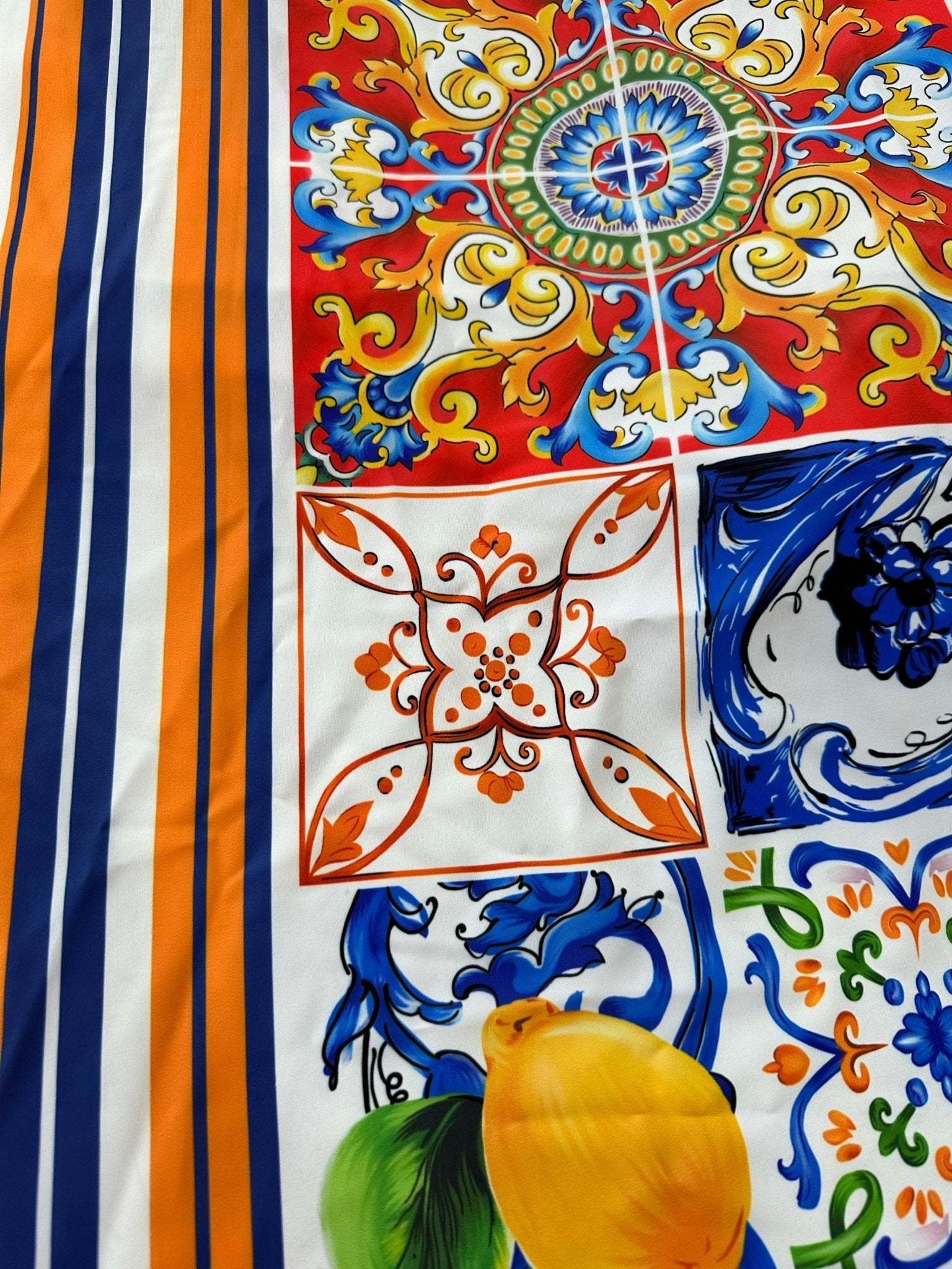 Sicilian print silky crepe fabric with vibrant orange, blue, and yellow decorative patterns and stripes