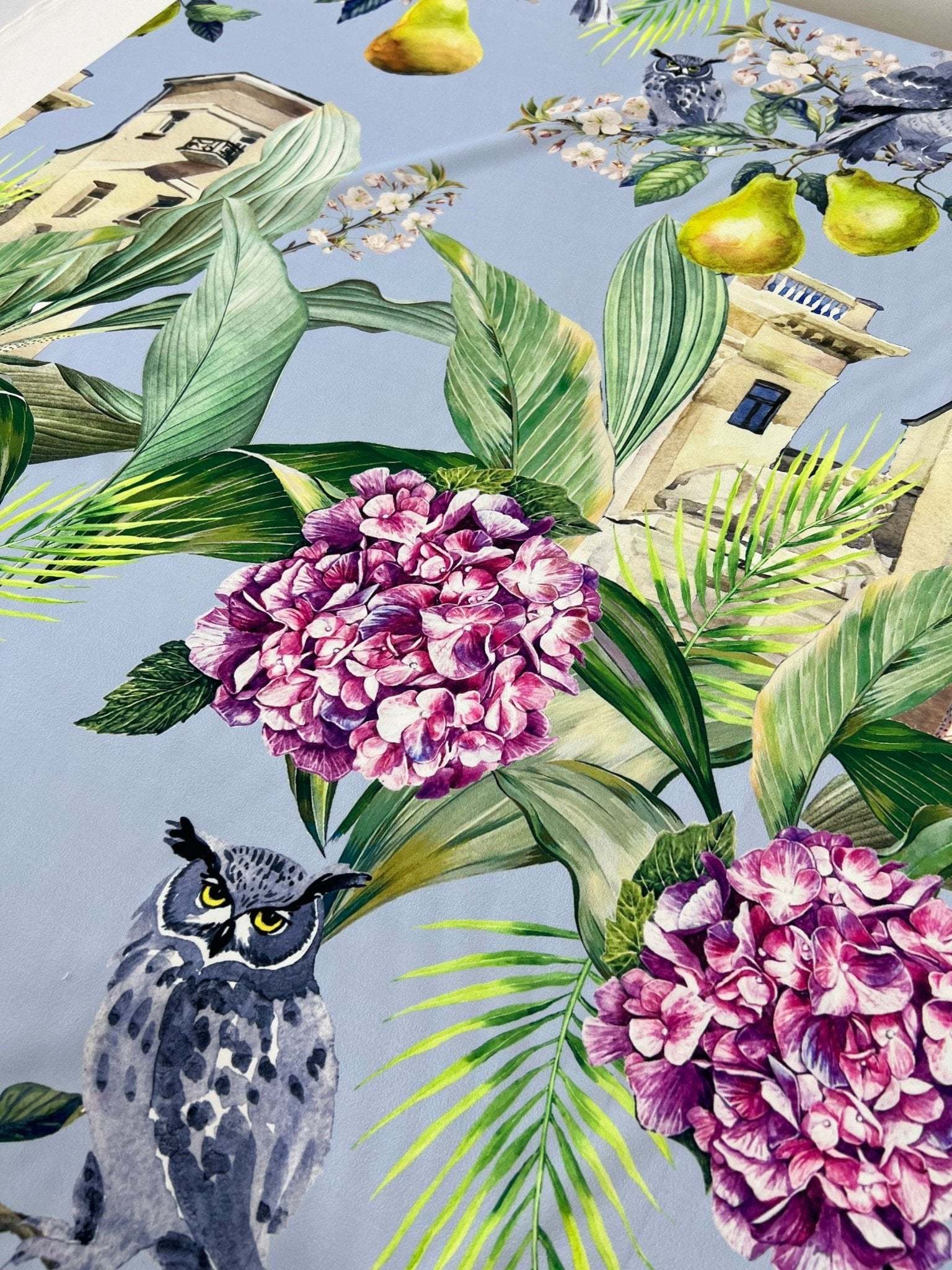Close-up of tropical parrot print crepe fabric with colorful flowers, leaves, and bird designs on a light blue background