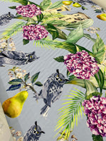 Tropical parrot print crepe fabric with vibrant parrots, pink flowers, and green leaves on a light background