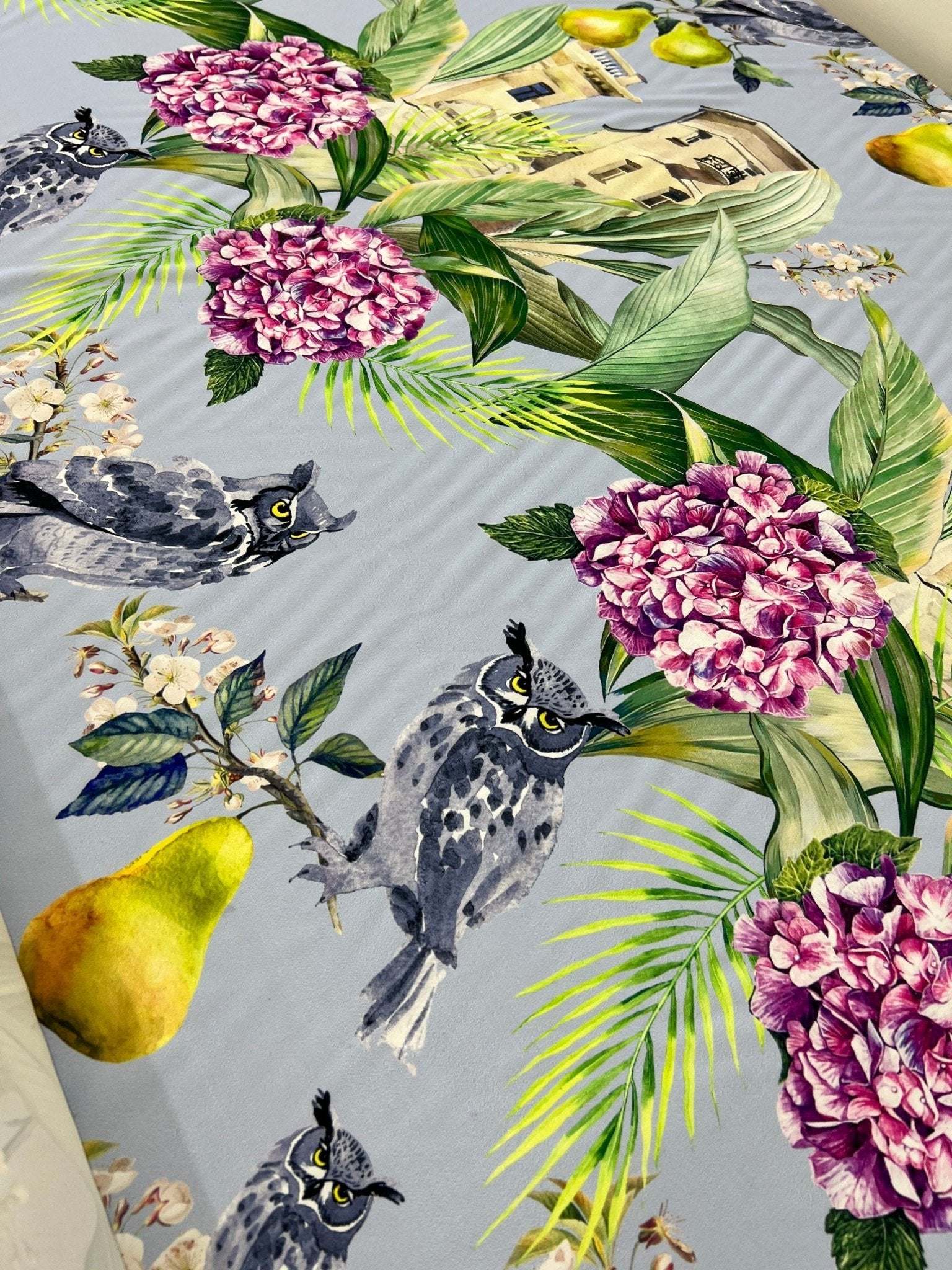 Tropical parrot print crepe fabric with vibrant parrots, pink flowers, and green leaves on a light background