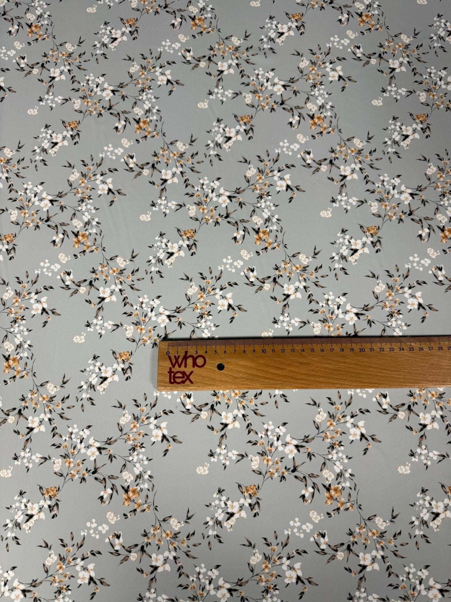 delicate cherry blossom print fabric with soft pastel floral pattern on light background and wooden ruler for scale