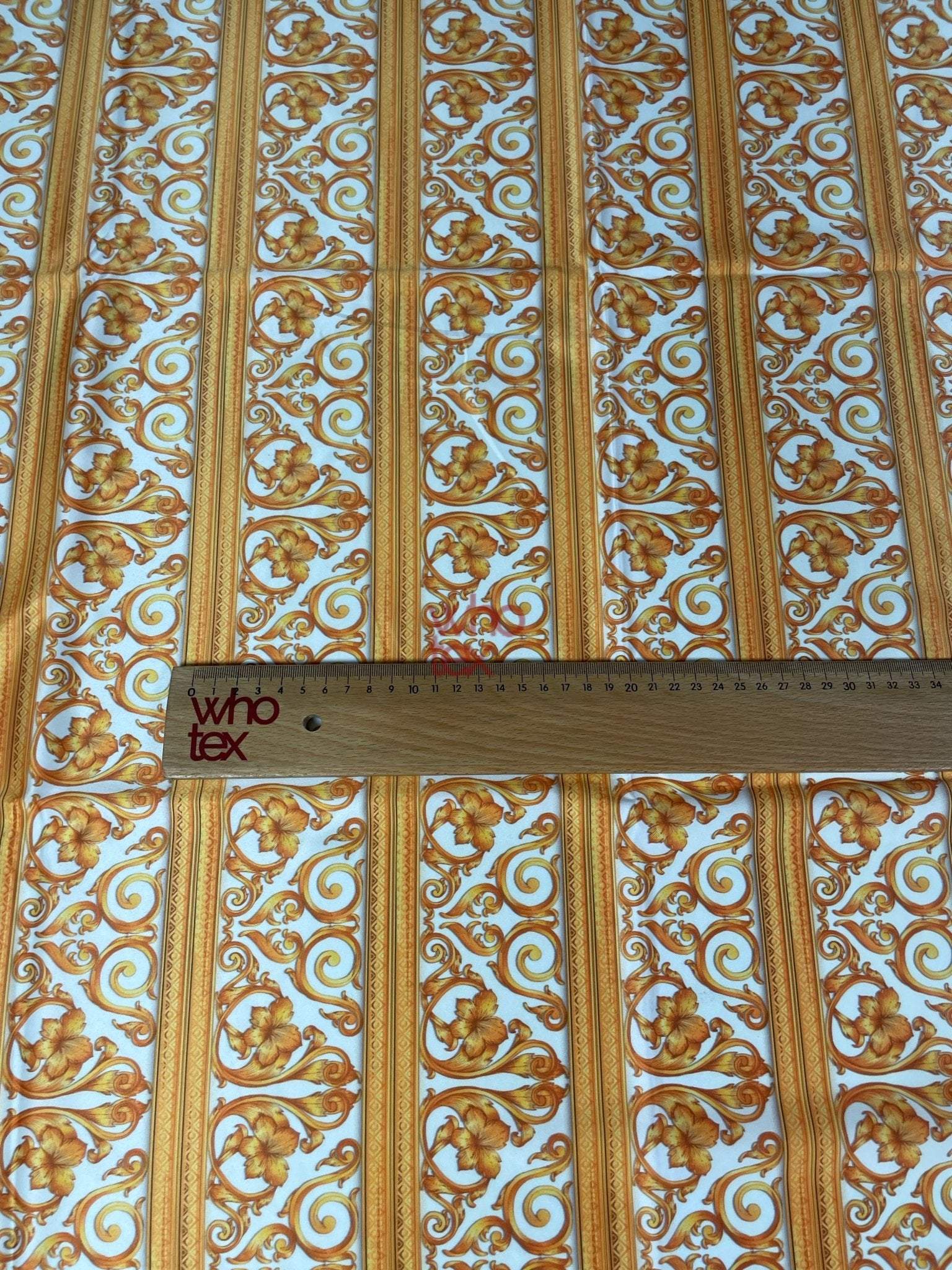 Elegant gold Baroque fabric with floral and scroll patterns and ruler for scale on white background