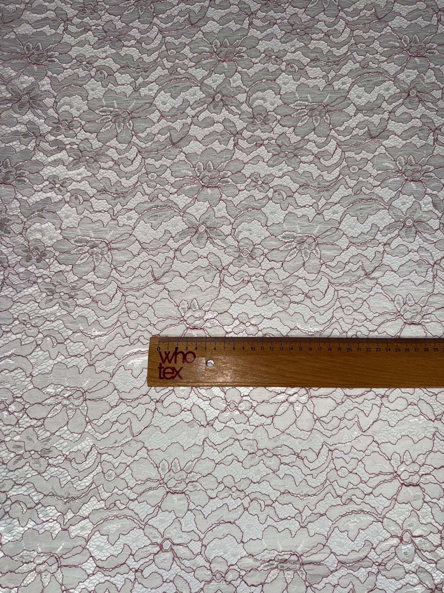 Elegant lace embroidered fabric with white and pink floral design and measuring ruler for scale
