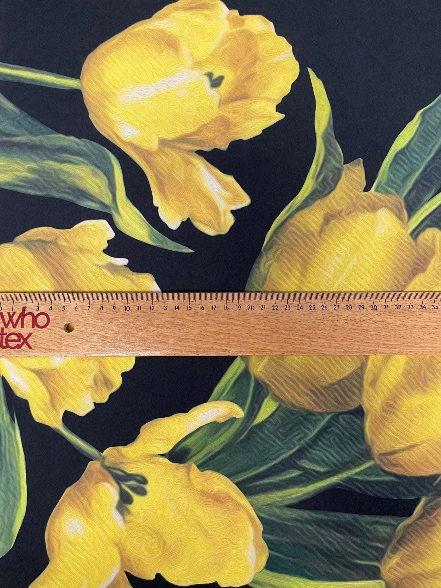 Elegant yellow tulip floral print fabric on black background with green leaves and wooden ruler for scale